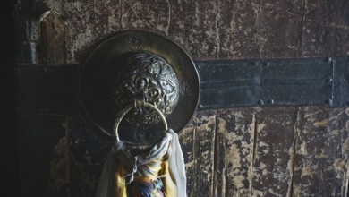 Detail of an old wooden door of a Buddhist monastery with metal ring and rope, surrounded by a