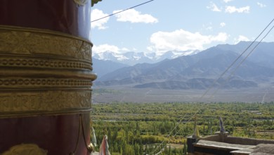 Large prayer wheel in foreground with view of snow-capped mountains and green valley, trekking in