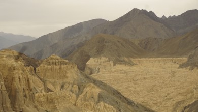 Wide mountain landscape with dramatic rock formations and valleys under a cloudy sky, trekking in