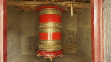 A large red prayer wheel decorated with decoration in a temple-like room, trekking in Ladakh,