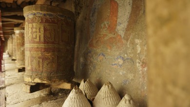 A series of ancient prayer wheels in front of a painted wall in a Buddhist temple, trekking in