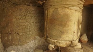 An ancient prayer wheel next to a wall full of inscriptions in a Buddhist context, trekking in