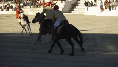 Polo players riding horses in a sand stadium in front of an audience in Leh, trekking in Ladakh,
