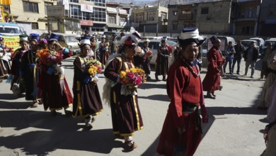 People wearing traditional garments carry flowers during a festive procession in Leh, trekking in