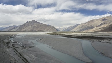 Extensive river landscape on the Indus with mountains in the background under a cloud cover,
