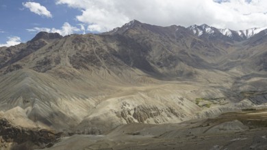 Dramatic mountain landscape with diverse rock formations, snow-capped peaks under a cloudy sky,
