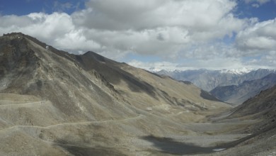 View of a rocky valley with winding mountain road and mountains in the background under slightly