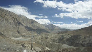 Wide mountain landscape with river valley and power lines under partly cloudy sky, trekking in