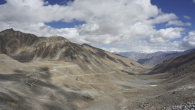 Wide mountain landscape with winding mountain road under a cloudy sky, trekking in Ladakh,