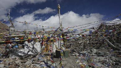 Colourful prayer flags surround a rocky area with statues at Khardug-La Pass and add color to the
