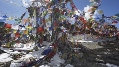 Sun shines through a jumble of colorful prayer flags over snow-covered ground at Khardung-La Pass I