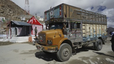 Colourful truck at Khardung-La Pass next to other vehicles and small houses with Indian flag under