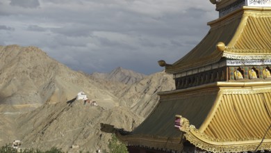 Roof of a Tibetan Buddhist temple with mountain backdrop and dramatic sky, trekking in Ladakh,