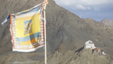 Tibetan Buddhist prayer flag with Namgyal Tsemo Buddhist monastery surrounded by mountains and sky,
