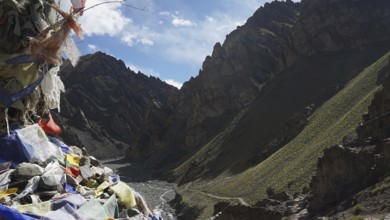 View of a valley with prayer flags and barren mountain landscape under blue sky, trekking at Stok