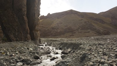 A stream flows through a dry, rocky landscape with high rock walls, trekking at Stok La Pass in