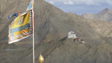 Colourful Buddhist flag with Namgyal Tsemo Buddhist monastery surrounded by mountains and sky, Leh,