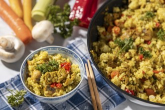 Bowl of fried rice and chopsticks next to pan and fresh ingredients