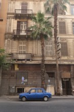 Cairo, Egypt. July 1st2024 A small blue car parked in an empty street of Downtown Cairo, with palm