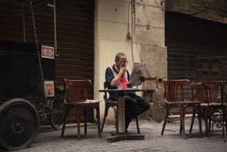 Cairo, Egypt. June 14th 2024 An Egyptian man smokes, drinks tea and reads a newspaper in local café