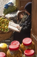 Cairo, Egypt. December 7th 2022 An Egyptian woman reading a book while selling fruit and vegetables