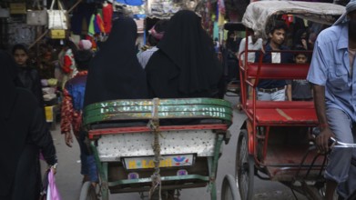 A hustle and bustle of rickshaws and people passing by on a narrow street in the Muslim quarter of