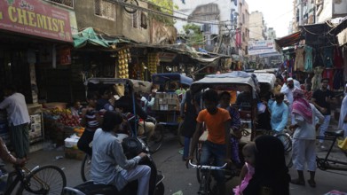 Bustling market street full of bicycle rickshaws and people in an urban area, Delhi, India