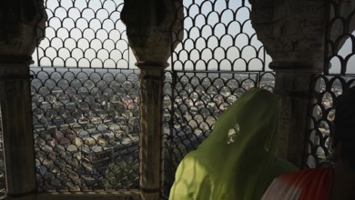 View of Delhi through an ornate grid from the mosque tower with two people in traditional dress,