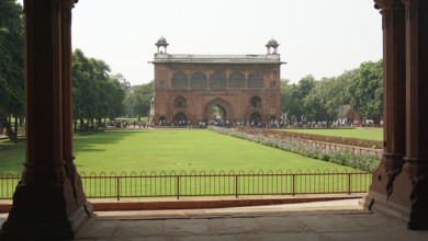 Historic gate with green lawn and trees, Red Fort in Delhi with numerous visitors in the area,