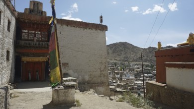 Houses and a colorful big prayer flag with mountains in the background under blue sky, Leh, city
