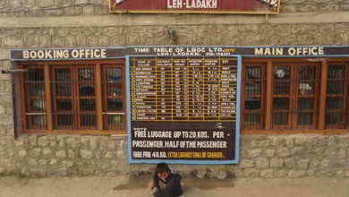 Stone building at the bus terminal with a large timetable on the façade and signs for Leh, Ladakh,