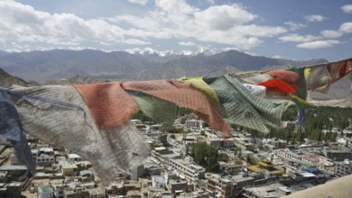 Prayer flags fly over Leh, a city with mountains and cloudy sky in the background, view from Leh