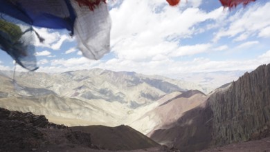 Prayer flags in front of a vast, cloud-covered mountain landscape, trekking at Stok La Pass in