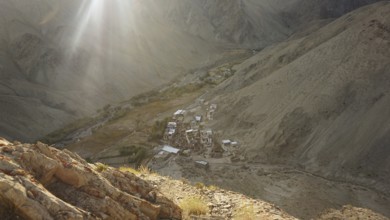 Rays of light illuminate a remote village in a valley between bare mountains, trekking in Ladakh,