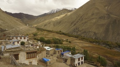 Small village in the valley with surrounding mountains and fields in the Himalayas, trekking in