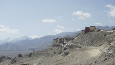 Building on a mountainous hill with a narrow road and blue cloud cover, Ladakh, Himalayas, India