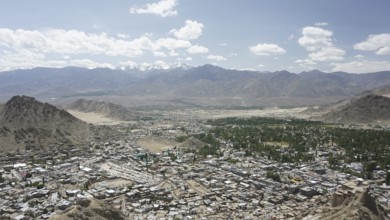 Long-range city view with mountains and sky in the background under white cloudy sky, Ladakh,