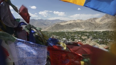 Colourful prayer flags in front of a vast valley and mountain landscape under clear skies, Ladakh,