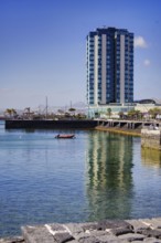Modern high-rise building reflected in calm water, urban ambiance under clear skies, Arrecife,