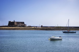 Historic Castillo de San Gabriel fortress by the sea, two boats on blue water under clear skies,
