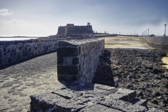 Stone path leads to the historic Castillo de San Gabriel fortress with a view of the sea under a
