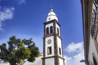 White church tower with clock of the Iglesia de San Ginés church under blue sky, surrounded by