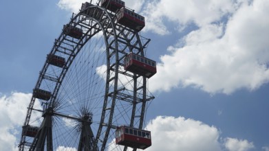 A big Ferris wheel with red cabins under a blue, cloudy sky, Prater, Vienna