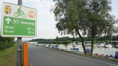 Signpost on Danube trail R1 with river and boats in the background, cycling on the Danube cycle