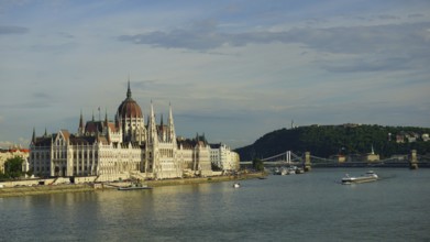 Large parliament building in Budapest on the banks of the Danube under blue sky with bridge in the