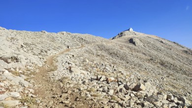 A trail snakes over a rocky mountainside up to the summit of Tahtali with clear skies, climbing
