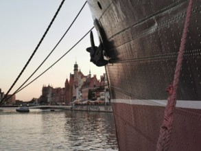 Looking along the bow, a large ship is moored in the harbor in front of the picturesque, historic