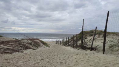Sandy trail through dunes with sea view and fences, cloudy sky, fresh spit, Baltic Sea, Poland