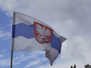 Polish flag with coat of arms and eagle in a close-up view against a partly cloudy sky, Poland