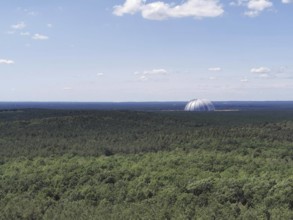 View of an extensive forest with the dome of Tropical Island, Cargolifter Hall on the horizon under
